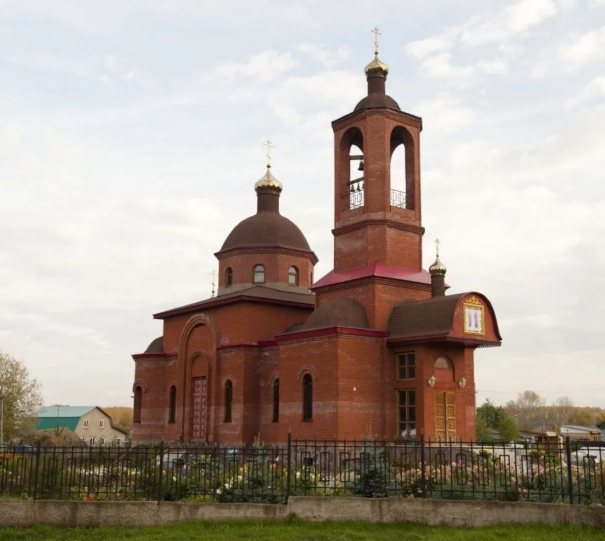 Краснокирпичный трёхглавый храм с колокольней на фоне неба