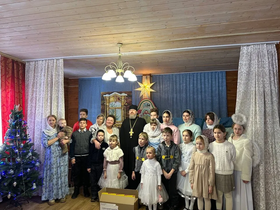 Дети в костюмах у наряженной ёлки и настоятель в зале воскресной школы