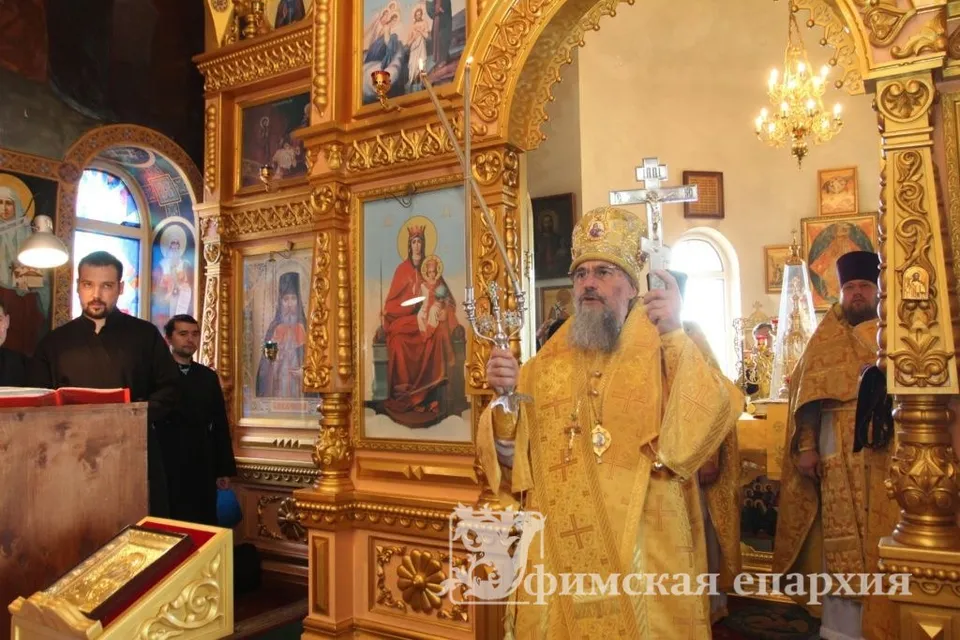 Золочёный иконостас с иконами Богородицы и святых, архиерей в жёлтом облачении на фоне иконостаса