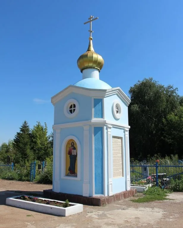 Небольшая голубая часовня с золочёным куполом среди деревьев кладбища