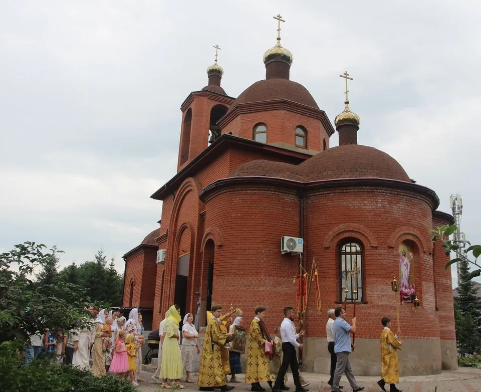 Крестный ход с хоругвями и иконой вдоль алтарной части краснокирпичного храма